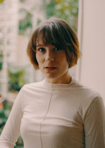 Eine junge Frau mit kurzen rotbraunen Haaren in weißem Rolllkragenshirt